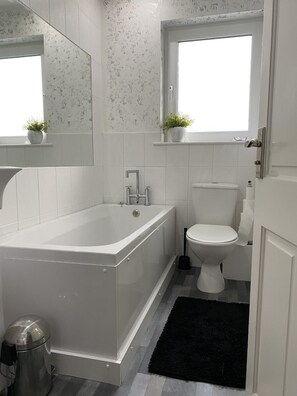 Une salle de bain moderne avec une baignoire sur pieds, des toilettes et une fenêtre située au-dessus des toilettes.