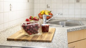 Keittiön työtasolla on leikkuulauta, jonka päällä on kulho täynnä rypäleitä sekä purkki hilloa, toinen kulho täynnä hedelmiä ja pesuallas.