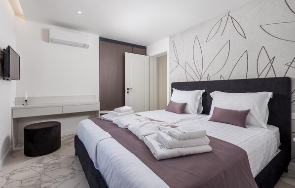 Una habitación de hotel moderna con una cama grande, una mesita de noche, un televisor de pantalla plana y un aire acondicionado de pared.