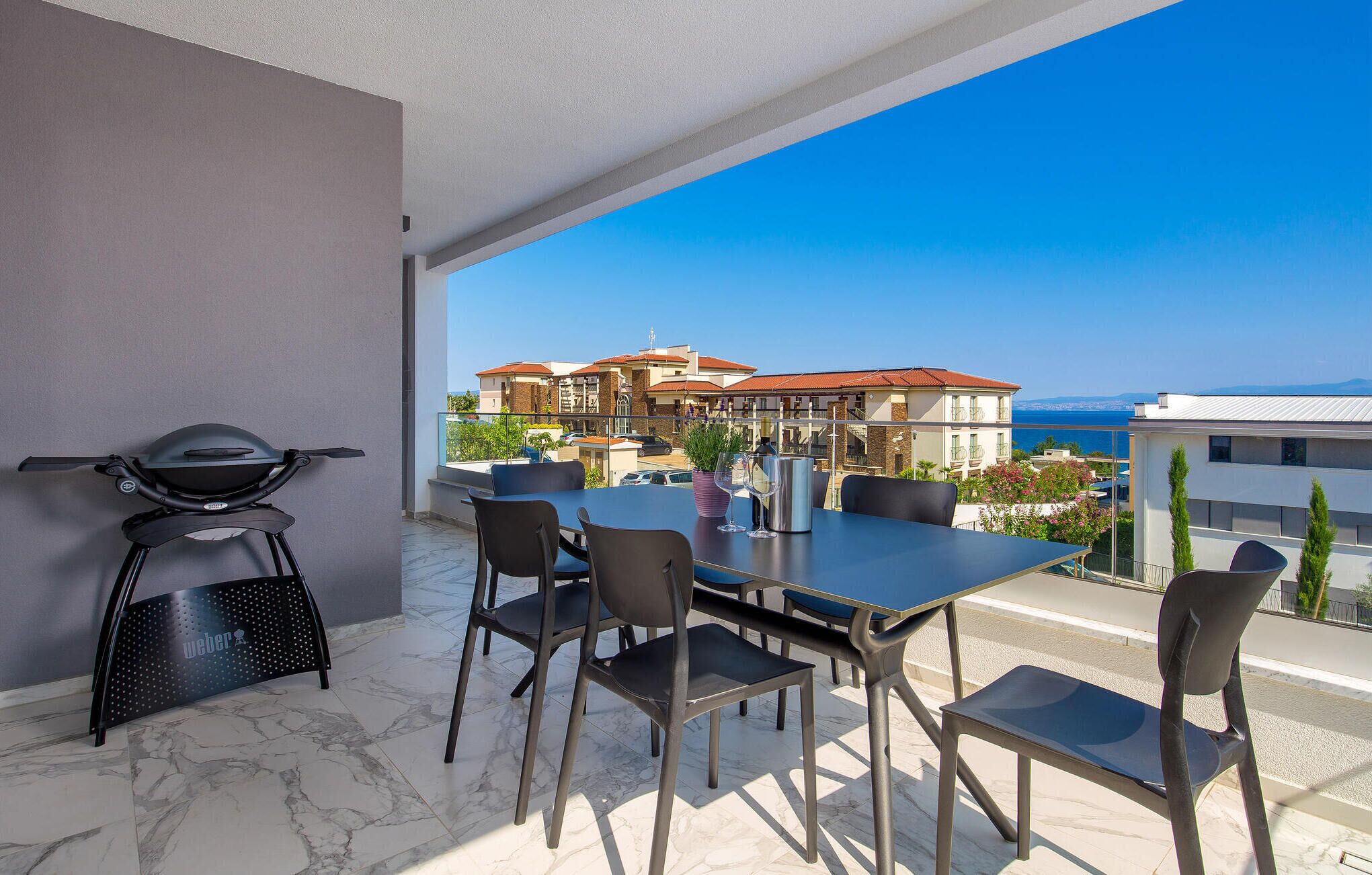 Ein Balkon mit Tisch, Stühlen, einem Grill und Blick auf Gebäude sowie das Meer.
