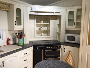 A compact kitchen with white cabinetry, a black stove, and a microwave.