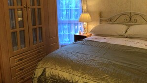 Un dormitorio con cama, mesita de noche, lámpara, ventana con cortinas y un armario de madera.