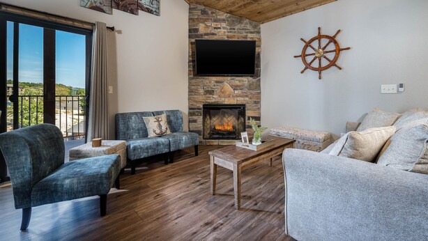 A cozy living room with a stone fireplace, a mounted TV, and a sail wheel decoration. - Boat Slip Included, Hot Tub, Lakefront resort (Branson)