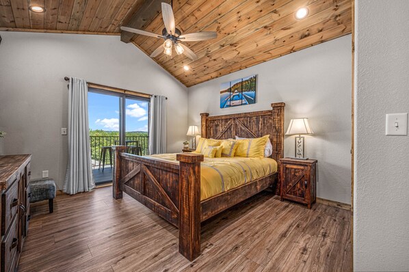 A bedroom with a wooden ceiling, a large bed with yellow bedding, two bedside lamps, and a view of greenery through a sliding door.
