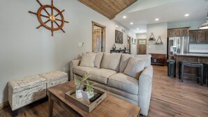 A living room with a sofa, a coffee table with a tray, a wooden bench, and a ship's wheel decoration on the wall. - Boat Slip Included, Hot Tub, Lakefront resort (Branson)