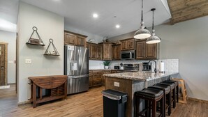 A modern kitchen with wooden cabinets, stainless steel appliances, a granite countertop, and a bar stool area. - Boat Slip Included, Hot Tub, Lakefront resort (Branson)