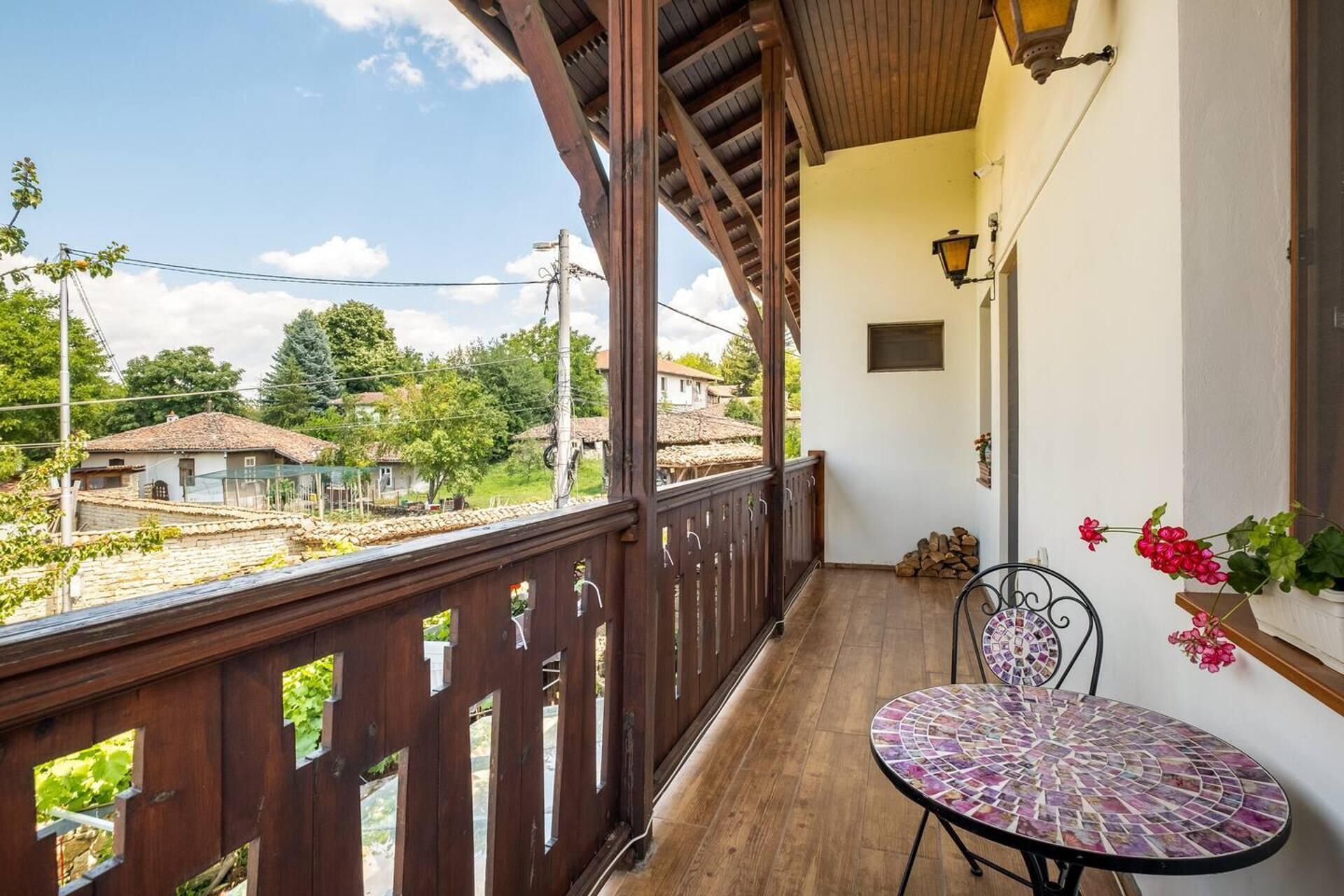 Un balcon doté d’une balustrade en bois, d’une table en mosaïque et offrant une vue sur des maisons et de la verdure.