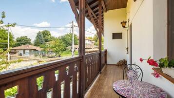 Un balcon doté d’une balustrade en bois, d’une table en mosaïque et offrant une vue sur des maisons et de la verdure.