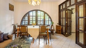 A dining area with a large table, chairs, a chandelier, and a view through arched windows. - Lovely 5-bed Authentic House in the Arbanasi (Veliko Tarnovo)