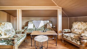 A cozy attic room with wooden walls and a sloped ceiling. It features a wooden table, two upholstered chairs, and a small round table with a decorative item. - Lovely 5-bed Authentic House in the Arbanasi (Veliko Tarnovo)