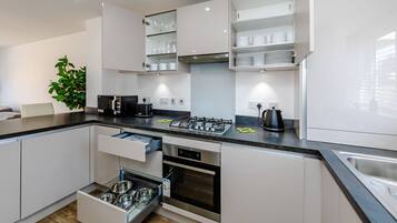 Une cuisine moderne avec des meubles blancs, un four encastré, une cuisinière à gaz et un évier.