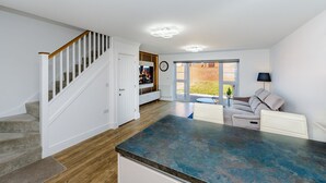 A spacious living area with a kitchen island, a staircase, and a sliding glass door leading to a patio. - My Chester Luxury 3bedroom Home (Colchester)