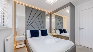 A modern hotel room with a large bed, bedside tables, a mirror, and a radiator. - My Chester Luxury 3bedroom Home (Colchester)