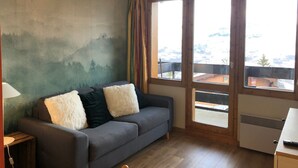 A room with a grey sofa, a lamp, and a view of snowy mountains through large windows. - Studio 4 Personnes Proche des Pistes (La Plagne-Tarentaise)