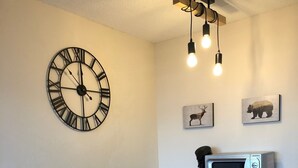 A compact kitchen with a white table, wooden chairs, a clock, a microwave, and a shelf with a basket and a decorative item. - Studio 4 Personnes Proche des Pistes (La Plagne-Tarentaise)