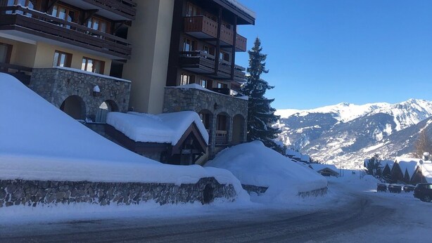 A multi-story building with wooden balconies and a stone facade, surrounded by snow-covered mountains. - Studio 4 Personnes Proche des Pistes (La Plagne-Tarentaise)