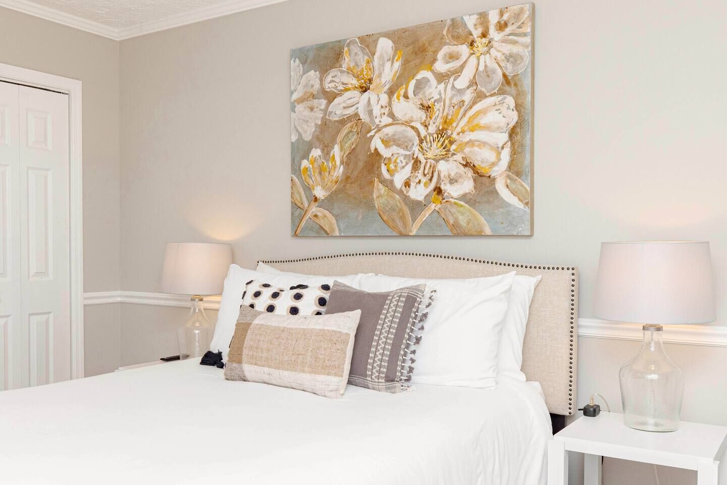 A bedroom with a large bed, two bedside tables with lamps, and a floral painting on the wall.