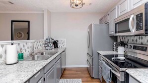 A compact kitchen with a sink, stainless steel appliances, and a patterned backsplash. - Comfort Stay | 2BR 2BA | Private Patio | Near RAFB (Warner Robins)