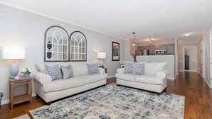 A living room with two white sofas, a patterned rug, and a kitchen in the background. - Comfort Stay | 2BR 2BA | Private Patio | Near RAFB (Warner Robins)