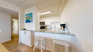 A modern kitchen with white cabinets, a granite countertop, and two bar stools. - Ocean View, Shared Pool/Hot Tub, Boardwalk to Beach (Port Aransas)