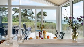 A dining area with a table set for two, overlooking a beach with trees and the sea.