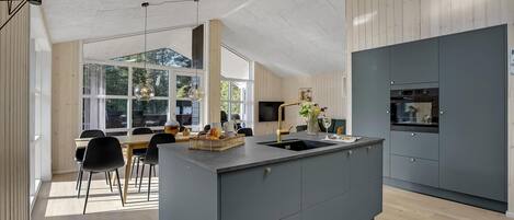 Een moderne keuken met een centraal eiland, ingebouwde apparatuur en een eethoek met natuurlijk licht.