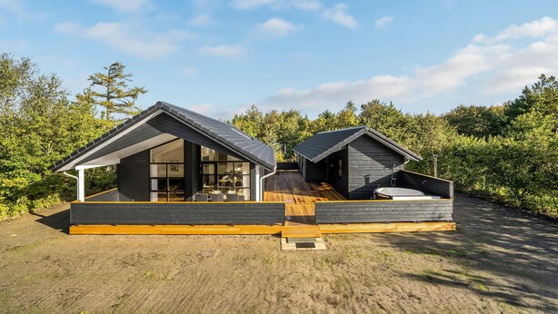 A modern cabin with a wooden deck, large windows, and a small outdoor hot tub.