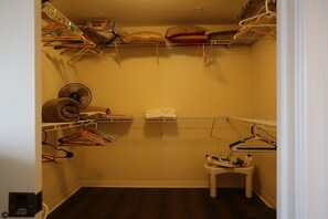 Un dressing avec plusieurs étagères, un ventilateur et un petit tabouret.