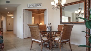 A dining area with a glass table surrounded by wicker chairs, a chandelier, and a mirror on the wall. - GRAND EXECUTIVE 3B/3B WATERSIDE 246 ISLAND CONDO (Fort Myers Beach)