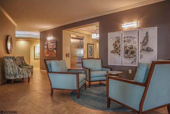 A lobby with a reception desk, a seating area with chairs, a large mirror, and artwork on the walls.