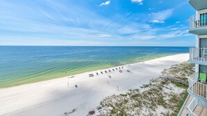 Une plage bordée d’un rivage de sable blanc, avec une eau d’un bleu limpide, et un bâtiment doté de balcons donnant sur la plage.
