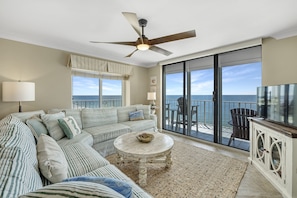 Relax in the spacious living area with a large sofa, coffee table, and sliding glass door leading to a balcony with ocean views.