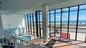 Un vaste espace intérieur doté de grandes fenêtres donnant sur une plage, une piscine et un escalier menant à un niveau supérieur.