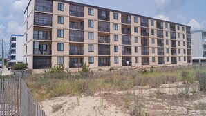 A multi-story hotel with balconies, located near a sandy area with sparse vegetation. - Bonaire 404-Oceanfront 126th St, Free WiFi, Elev, W/D, AC (Ocean City)
