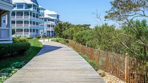 A wooden boardwalk leading to a multi-story building with balconies. - Sunset Island-Fountain Dr 37 #5A-Bayside 67th St, WIFI, Pools, Elev, W/D, AC (Ocean City)