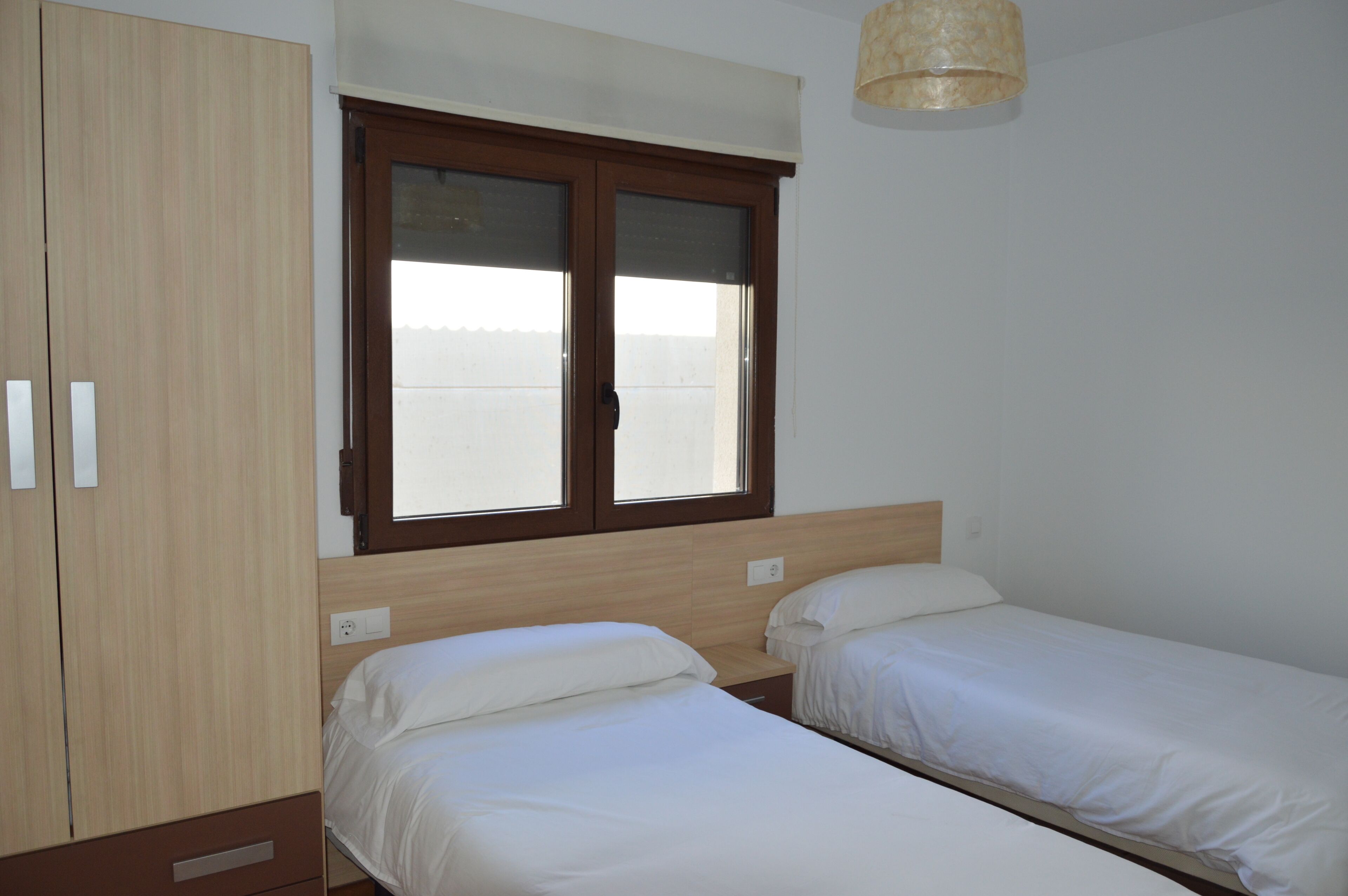 Een slaapkamer met twee eenpersoonsbedden, een houten garderobe en een raam met zonwering.