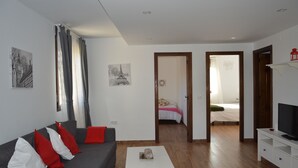 A modern living room with a grey sofa, red and white cushions, a white coffee table, and a TV on a white stand.