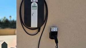 A wall-mounted EV charging station with a cable connected to a wall socket.