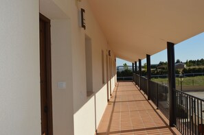 A covered balcony with tiled flooring, black railings, and a clear view of the surrounding landscape.