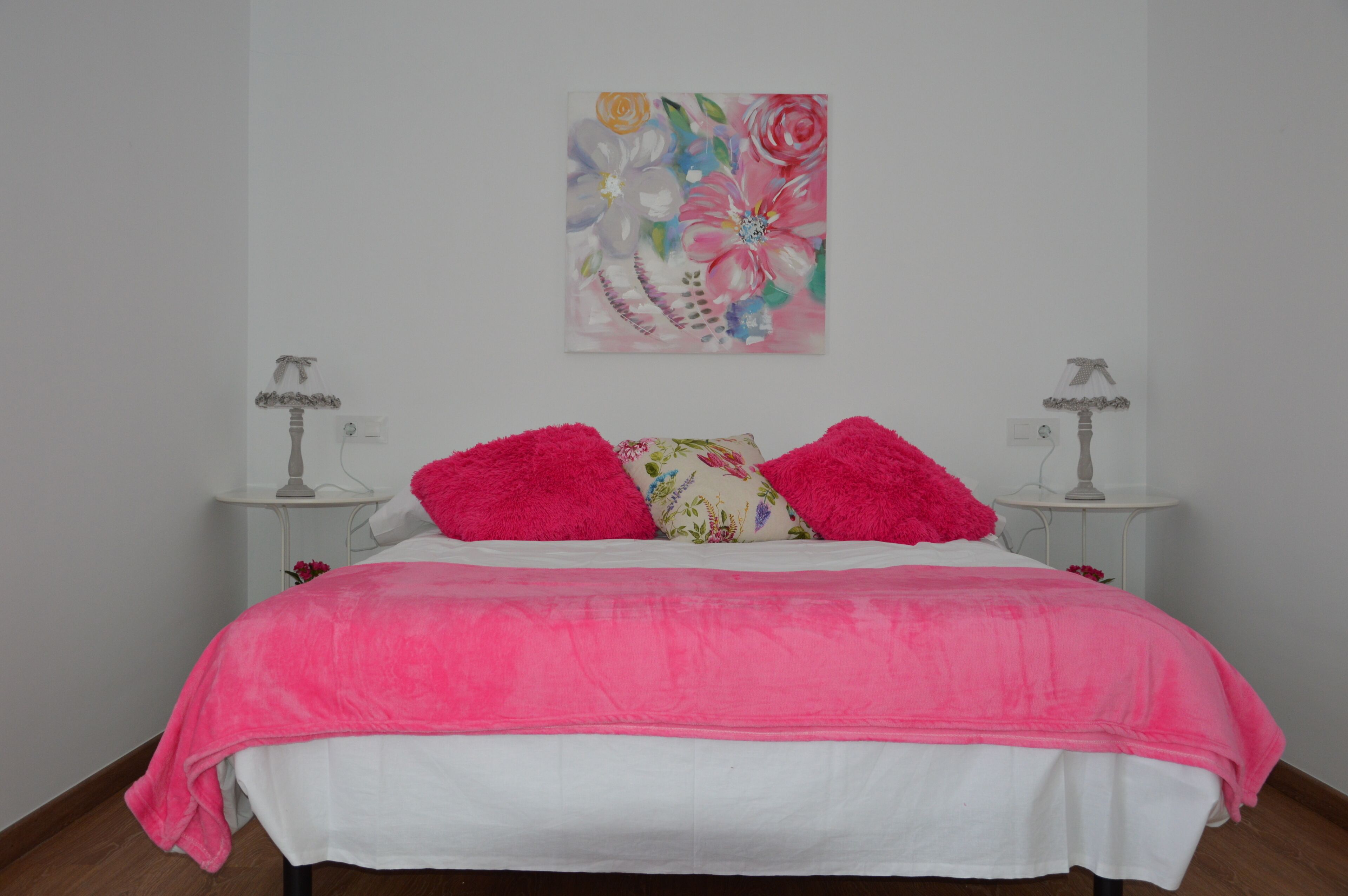 A bedroom with a bed, two bedside tables, and a floral artwork on the wall.