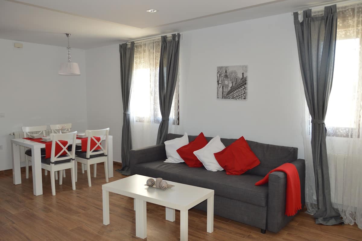 A living room with a grey sofa, white chairs, a white coffee table, and grey curtains.