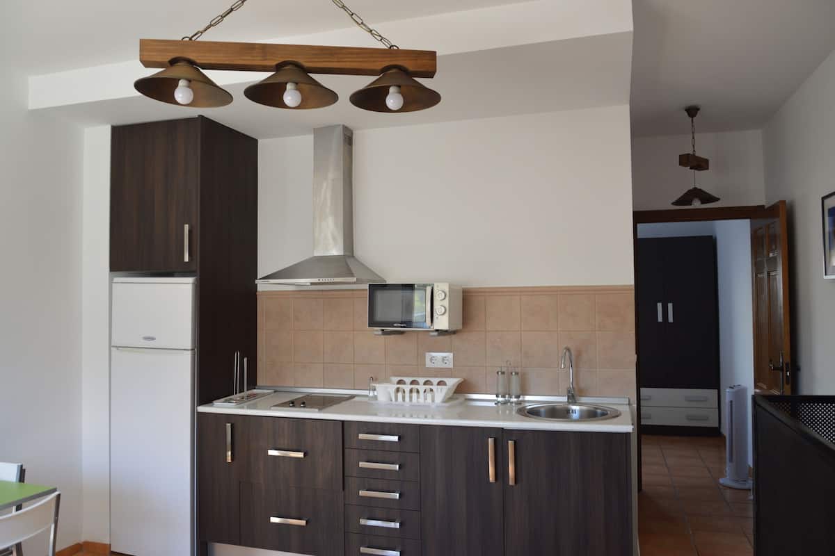 A modern kitchen with dark wood cabinets, a white countertop, a microwave, and a stainless steel sink.