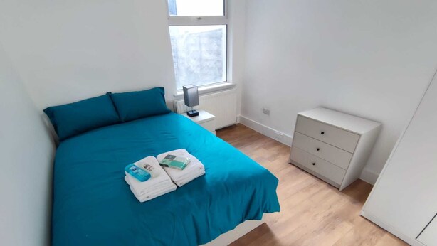 Une chambre à coucher avec un grand lit, une table de chevet, une commode et une fenêtre.