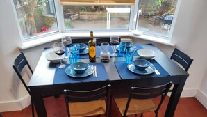 Une table à manger dressée pour quatre personnes, avec de la vaisselle en verre bleue, une bouteille de vin et une vue sur la fenêtre.