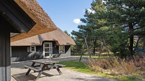 A rustic building with a thatched roof, a wooden picnic table, and a swing set in a natural setting. - Stunning home in Blåvand with sauna (Blåvand)