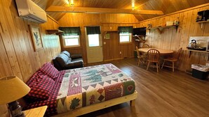 Een knus vakantiehuisje met houten inrichting, een bed met sprei, een eettafel met stoelen en een kitchenette.