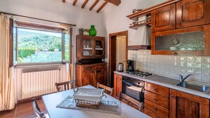 A kitchen with wooden cabinets, a dining table with chairs, a window with curtains, and a view of a garden. - Gorgeous home in Arezzo with kitchen (Arezzo)
