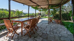 An outdoor patio with a stone floor, wooden furniture, and a pergola with a thatched roof. - Gorgeous home in Arezzo with kitchen (Arezzo)