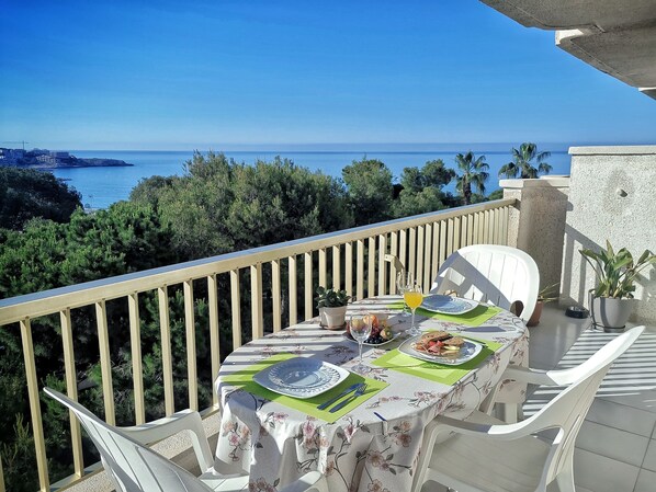 A balcony with a table set for two, overlooking a coastal view.