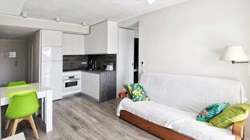 Un espacio habitable compacto con kitchenette, comedor y sofá con cojines.